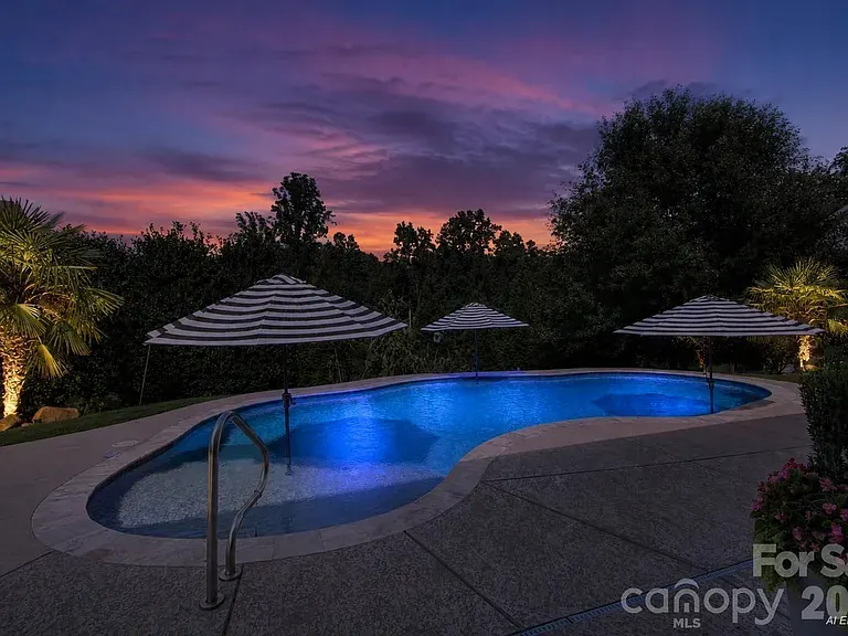 Backyard pool lit up at sunset, with striped umbrellas